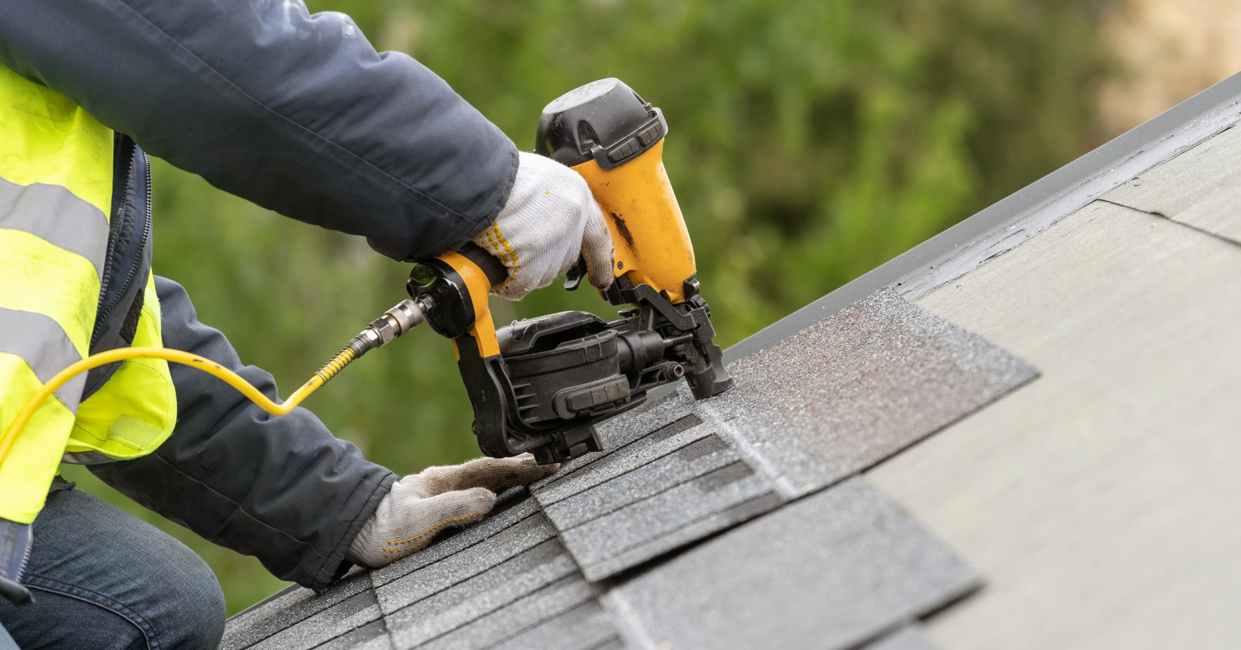 Worker using nail gun on roof shingles